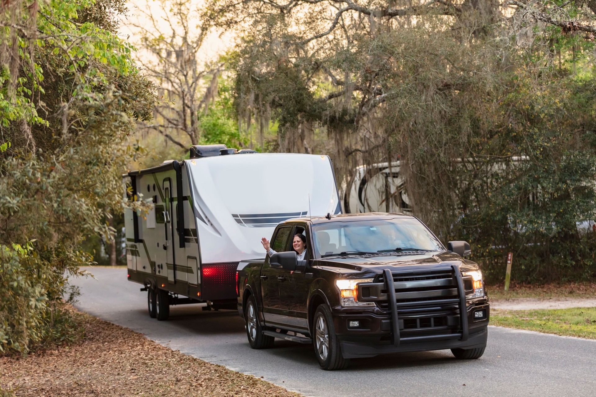 Couple driving camper trailer on rural road, woman waving